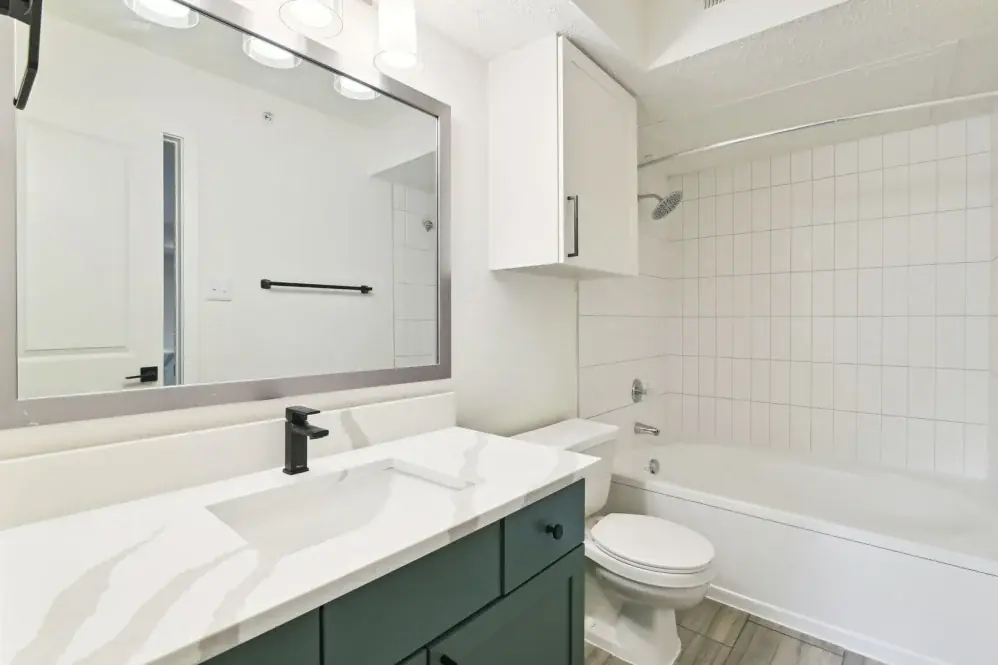 Finished bathroom with a green vanity, white counter, framed mirror, and tiled tub surround